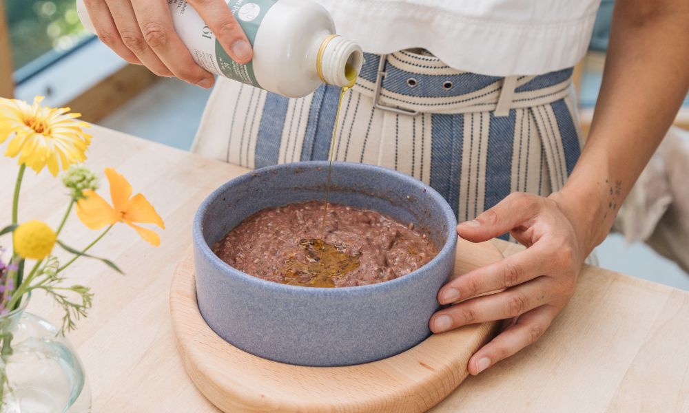 Grauer, großer Hund, der aus Napf frisst. Der Napf steht auf einer weißen Bank, daneben stehen 2 Futtertüten und eine Blume.