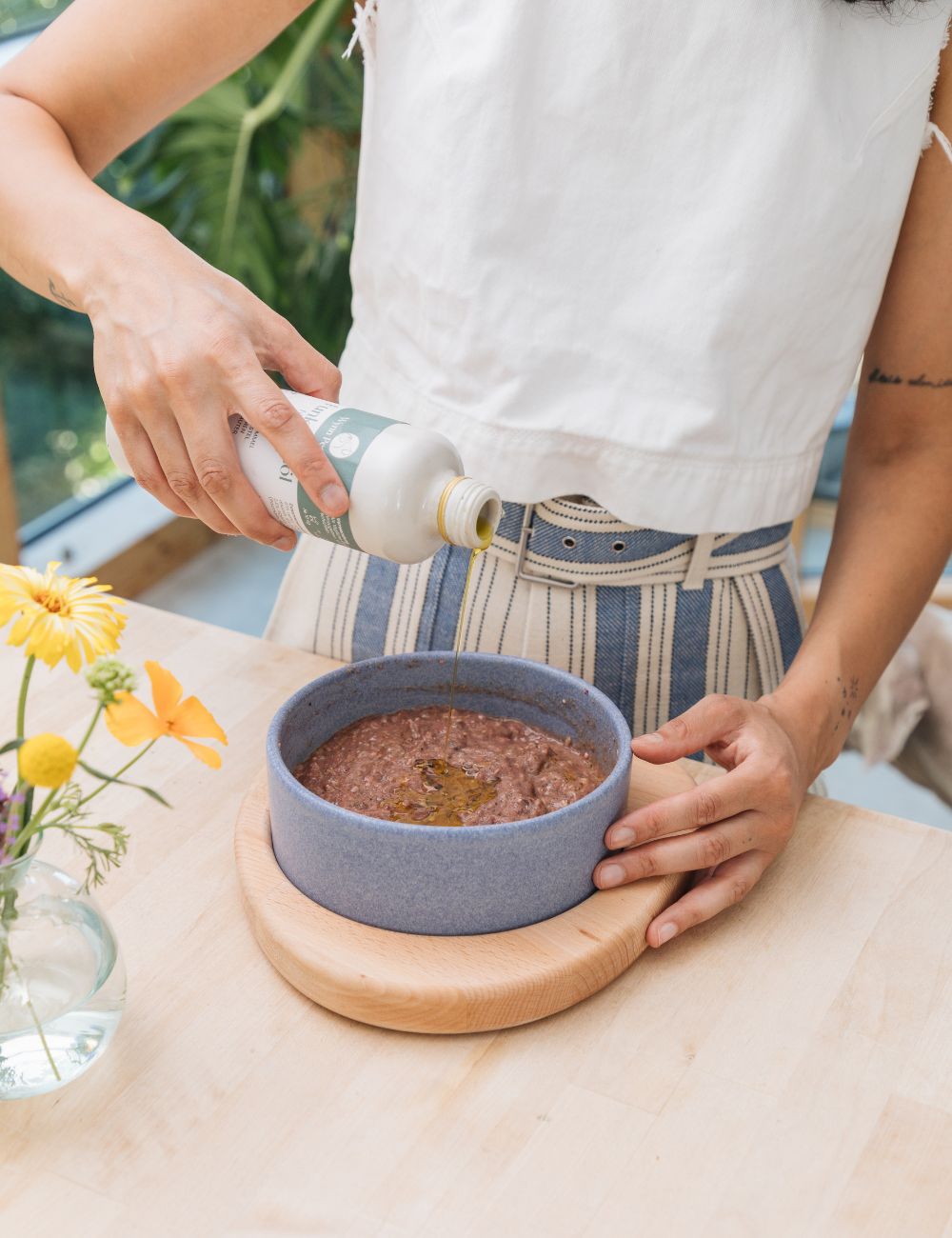 Futtertüte, die gerade in Napf ausgekippt wird. Der Napf hat einen Untersetzer aus Holz.
